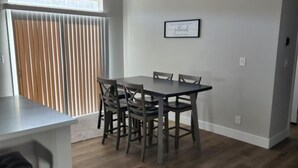 Un comedor con una mesa y sillas, una encimera de cocina y un ventanal con persianas.