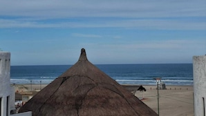 A beach view with a thatched-roof structure in the foreground and a lifeguard tower in the background.