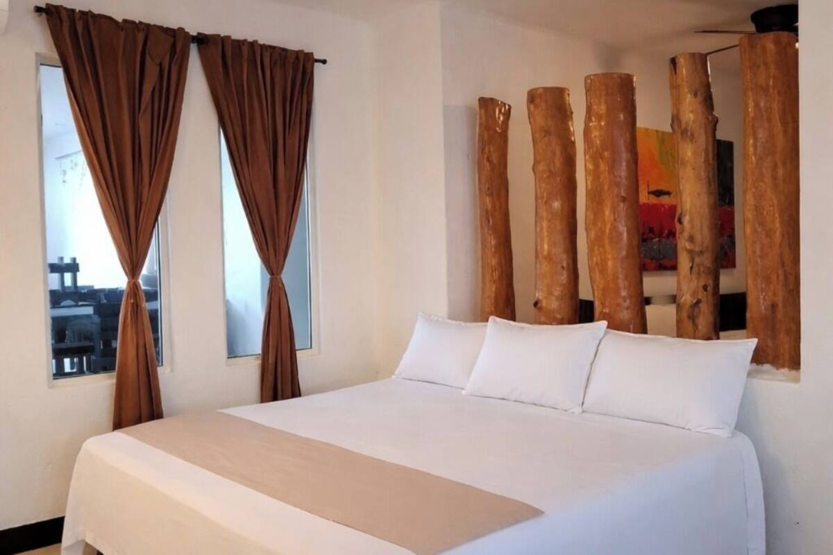 A large bed with white linens, a brown accent runner, and two brown curtains.