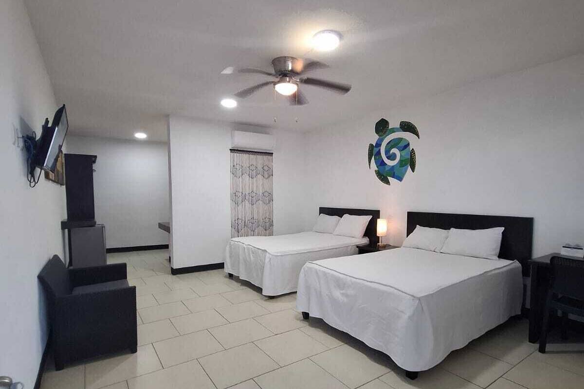 A hotel room with two beds, a ceiling fan, a TV mounted on the wall, and a decorative wall piece.