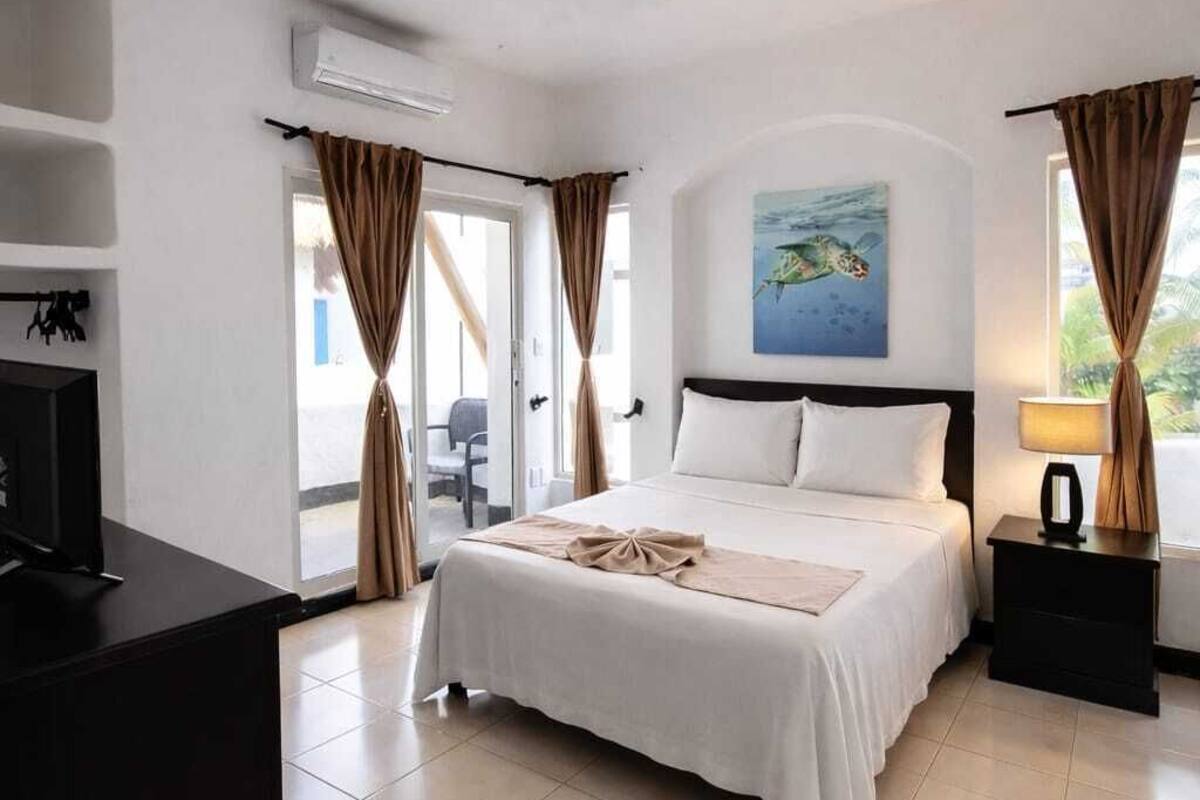 A hotel room with a bed, a desk, a ceiling fan, and a window with curtains.
