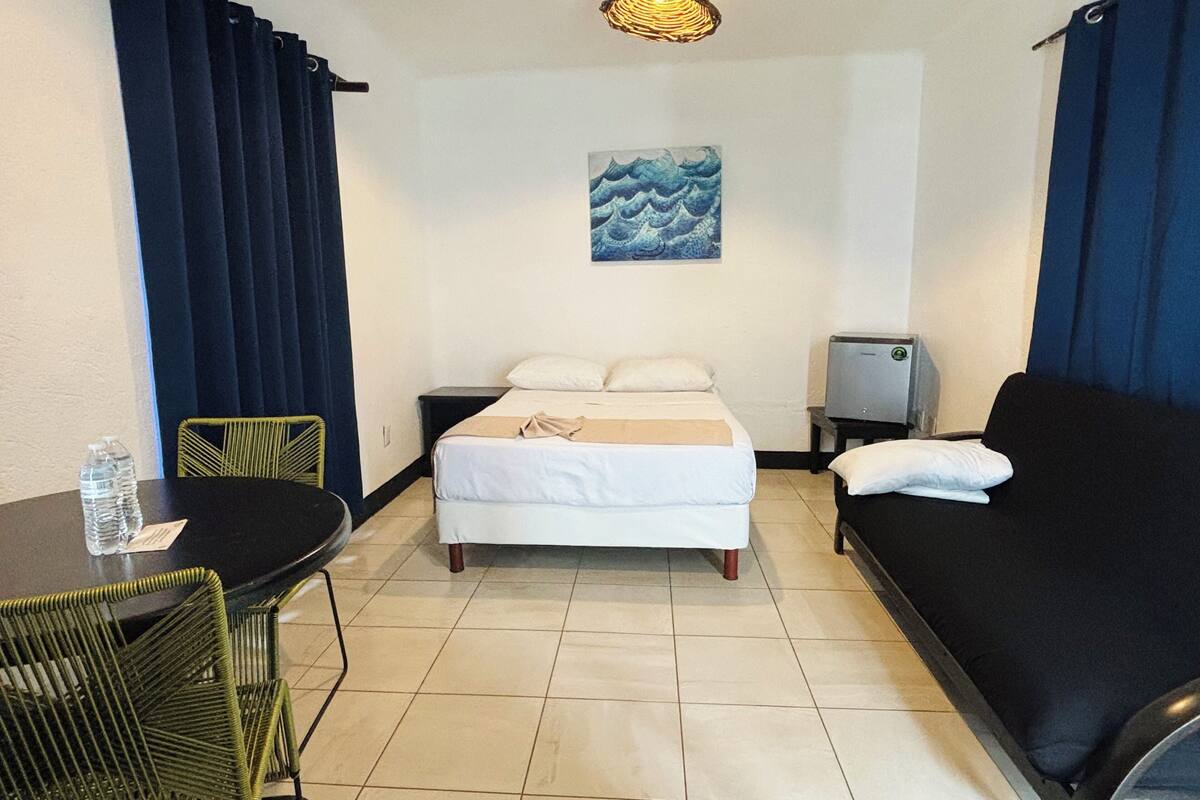 A hotel room with a bed, a sofa, a table with chairs, a TV, and a painting on the wall.