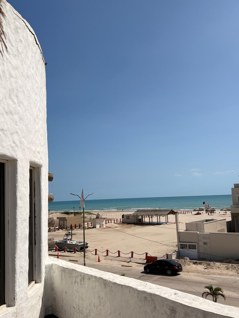 Vista costera con cielo despejado, una playa y un edificio con balcón que domina el mar.