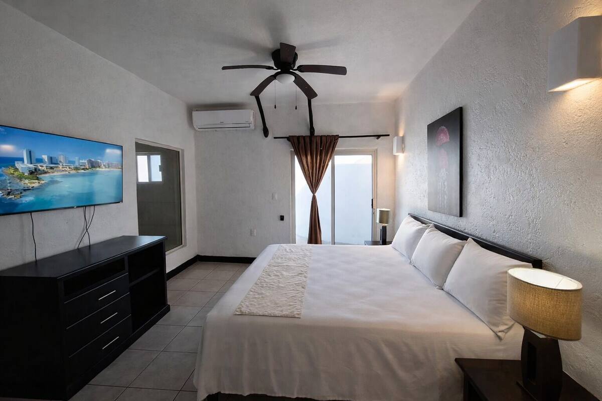 A hotel room with a bed, a TV, a ceiling fan, a window, and a door.