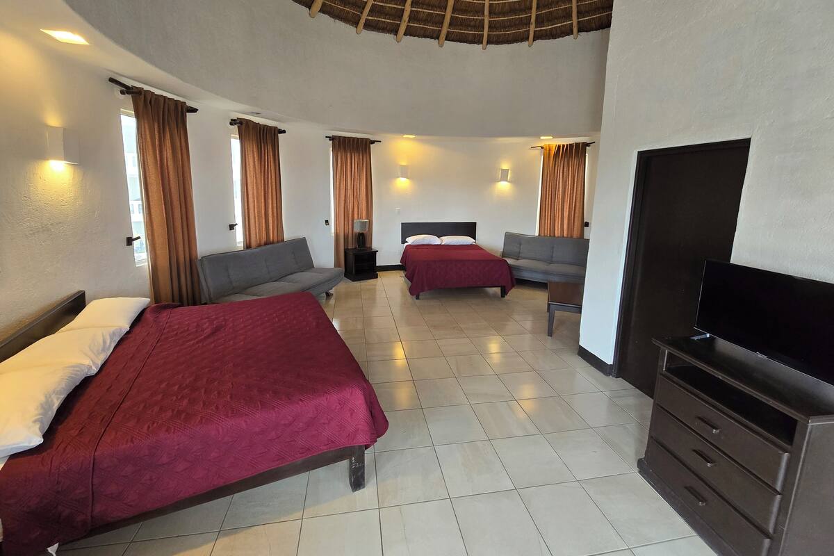 A hotel room with two beds, a sofa, a TV, and a ceiling fan.