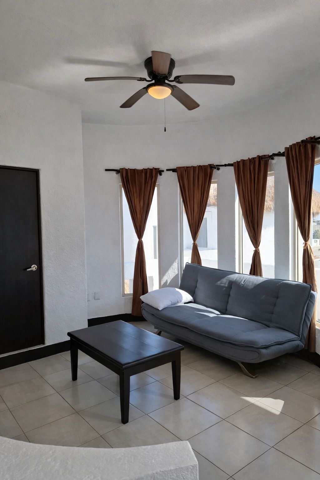 A living room with a sofa, a coffee table, a ceiling fan, and curtains on the windows.