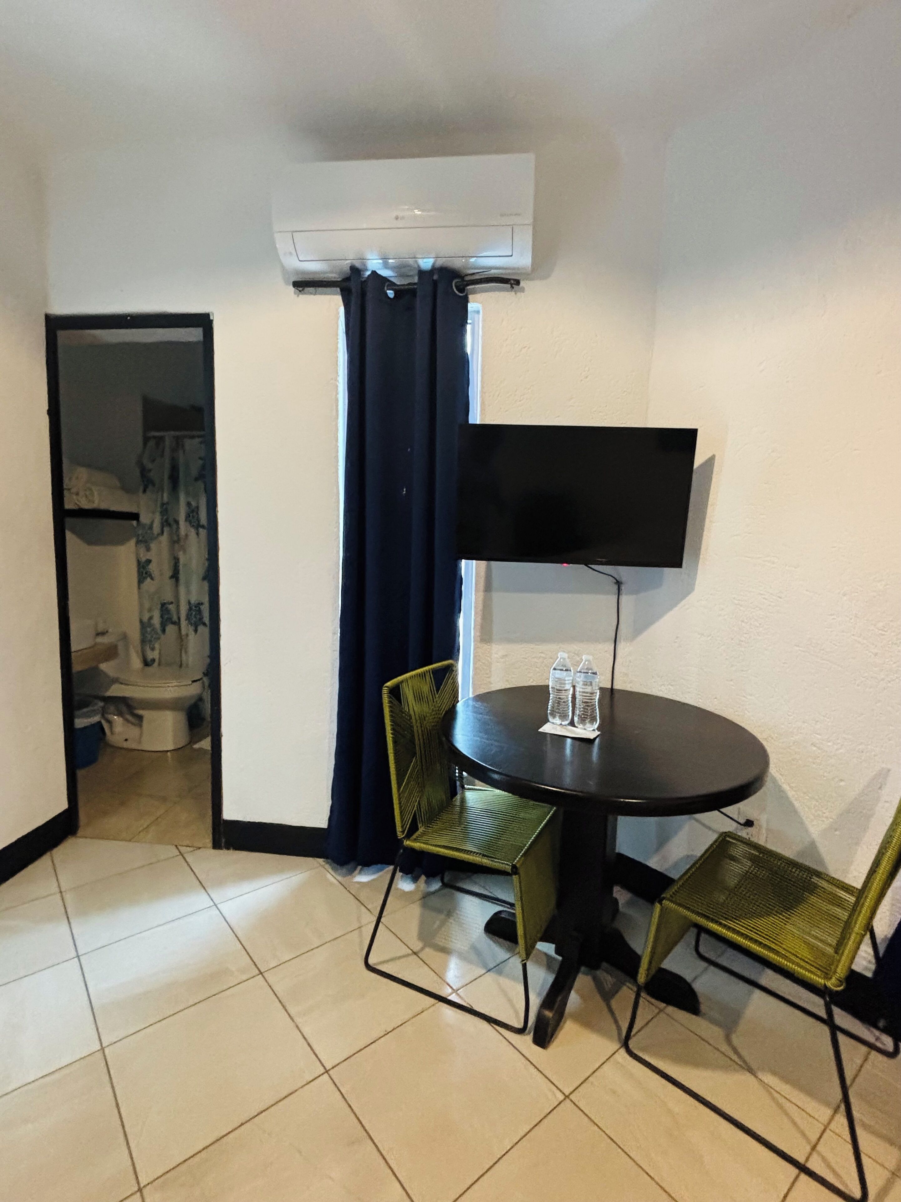 Una habitación pequeña con una mesa redonda, dos sillas, un televisor de pantalla plana y un equipo de aire acondicionado.
