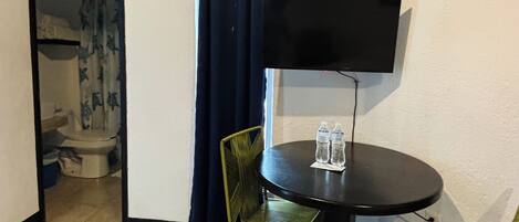 Una habitación pequeña con una mesa redonda, dos sillas, un televisor de pantalla plana y un equipo de aire acondicionado.