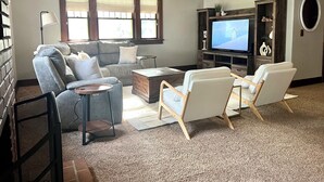 En stue med sofa, to lænestole, sofabord, fjernsyn og loftventilator.