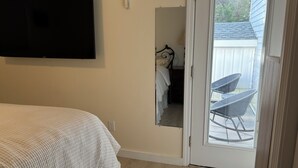 Une chambre avec un lit, un téléviseur fixé au mur et une porte-fenêtre coulissante donnant sur une terrasse extérieure avec une chaise.