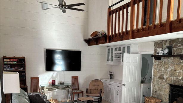 Un vaste salon doté d’un haut plafond, d’un ventilateur de plafond en bois, d’un téléviseur à écran plat fixé au mur, d’une cheminée en pierre et d’un escalier en bois.
