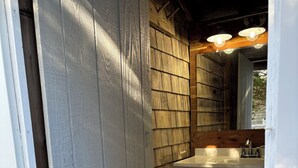 Une façade en bois avec une porte blanche, une petite fenêtre et un lavabo blanc surmonté d’un miroir.