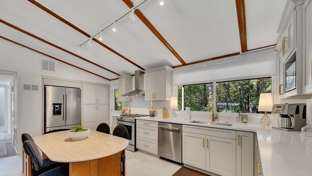 A modern kitchen with a central island, stainless steel appliances, and a view of greenery outside.