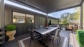 An outdoor patio with a dining table and chairs, a small potted plant, and a view of a house in the background.