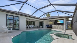 A modern indoor pool area with clear water, a glass ceiling, and a seating area with white chairs. - Heated Pool | Hot Tub | Game Room | Gulf Access (Cape Coral)