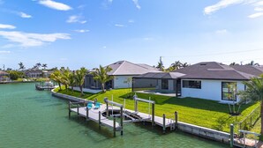 A waterfront property with a dock, a pool, and a well-maintained lawn. - Heated Pool | Hot Tub | Game Room | Gulf Access (Cape Coral)