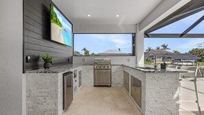 A modern kitchen with a large island, built-in appliances, and a view of the outdoors. - Heated Pool | Hot Tub | Game Room | Gulf Access (Cape Coral)