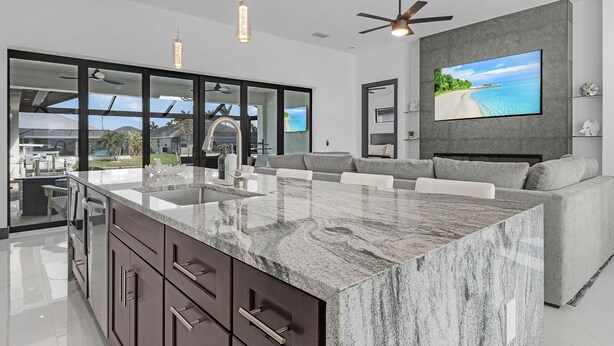 A modern kitchen with a large island, a built-in oven, and a dining area with a view of the outdoors. - Heated Pool | Hot Tub | Game Room | Gulf Access (Cape Coral)