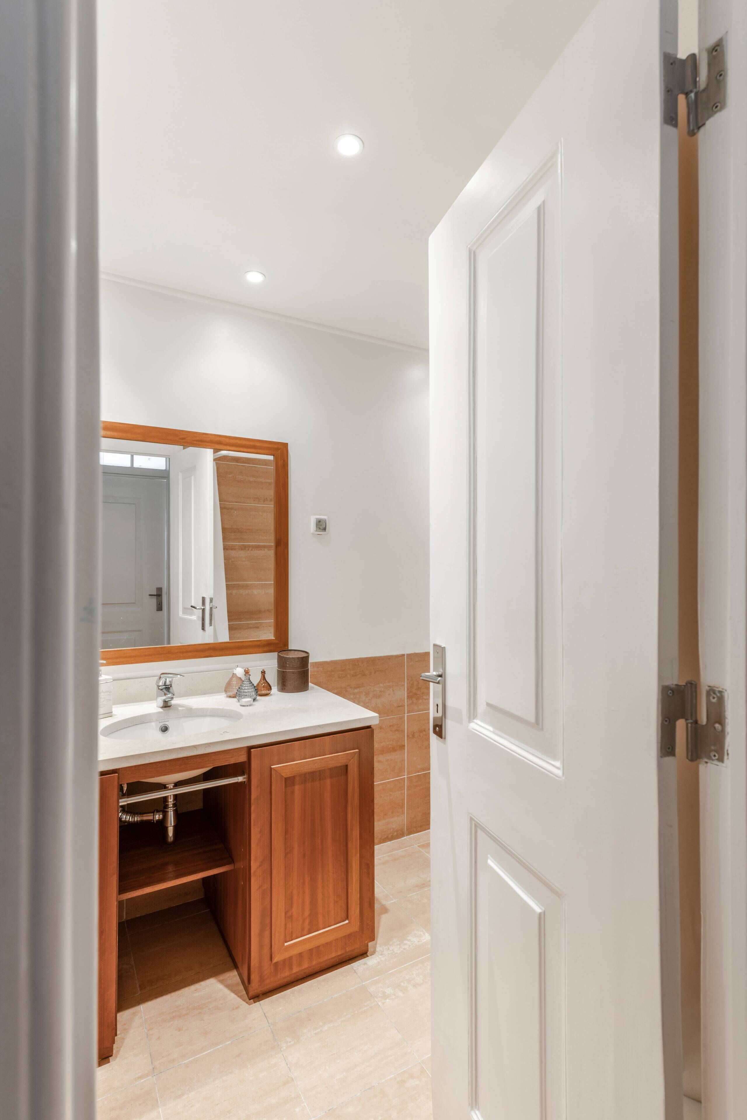 Une salle de bain avec un lavabo blanc, un meuble en bois et un grand miroir.