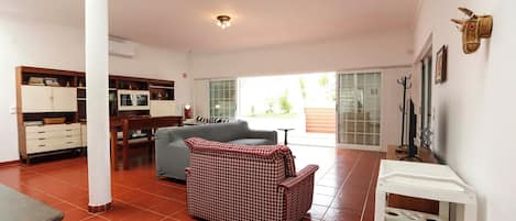 Amplia sala de estar con sofá, mesa de comedor y zona de cocina con armarios y televisor.