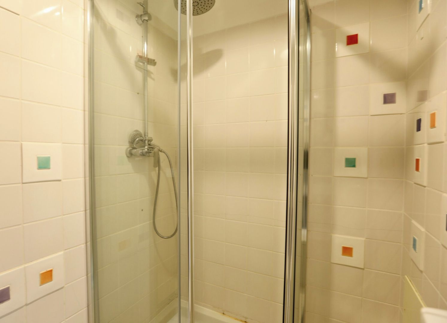 A glass-enclosed shower area with a handheld showerhead and a wall-mounted control panel.