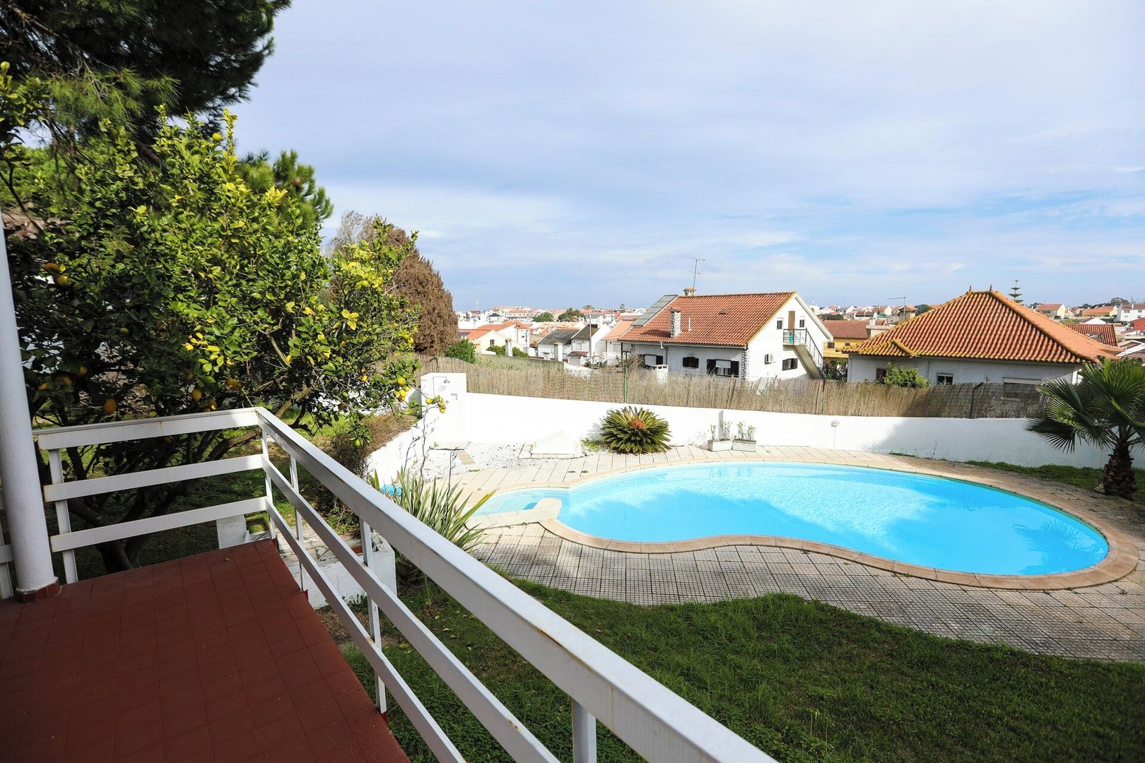 A residential area with a swimming pool, a white fence, and houses with red-tiled roofs.