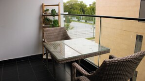 Een balkon met een glazen tafel en rieten stoelen, met uitzicht op een tuin en een gebouw.
