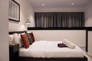 A neatly made bed with white bedding and a brown headboard, a bedside table with a lamp, and a framed picture on the wall.
