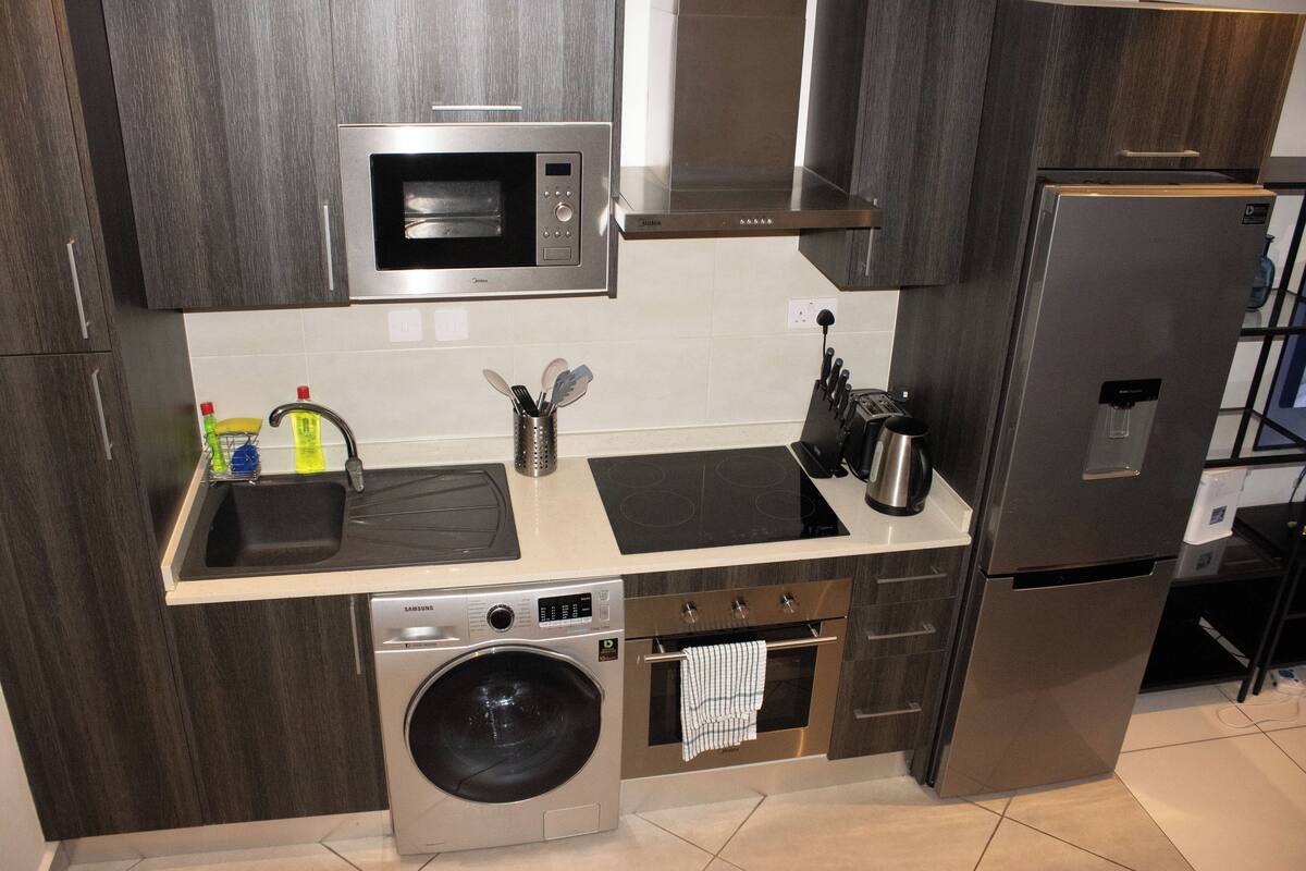 A modern kitchen with stainless steel appliances, a built-in washing machine, and a compact layout.