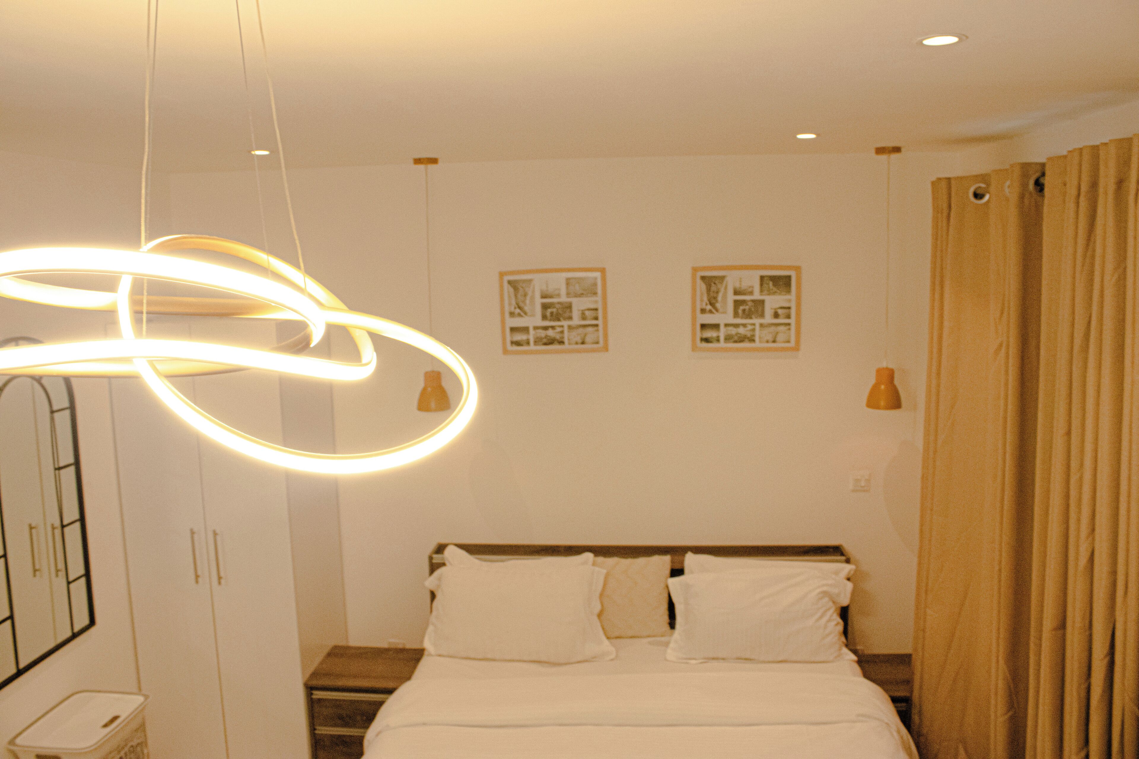 Een moderne slaapkamer met een bed, een hanglamp en twee ingelijste foto’s aan de muur.