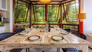 Mesa de comedor para seis personas con vistas a un follaje exuberante a través de grandes ventanales.