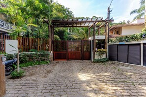 Una entrada empedrada con una puerta de madera, rodeada de abundante vegetación y una valla de metal.
