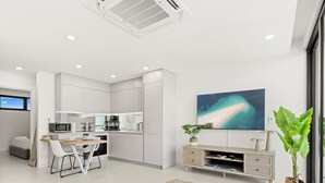 Une cuisine moderne et bien éclairée, avec des meubles blancs, un coin repas doté de chaises blanches et un grand tableau abstrait accroché au mur.