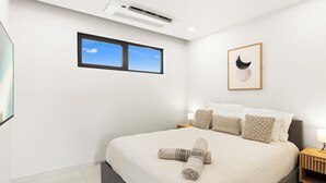 Une chambre moderne avec un grand lit, une fenêtre, un appareil de climatisation et une œuvre d’art encadrée accrochée au mur.