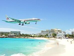 An airplane with the American Airlines logo flying over a beach with clear turquoise water and a hotel in the background. - A124 - Wonderfull 3 bedrooms with amazing view (Sint Maarten)