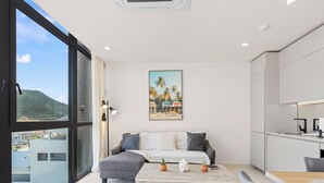A modern living room with a sofa, coffee table, and a painting of a beach scene. - A123 -  1 bedroom with paradise view (Sint Maarten)