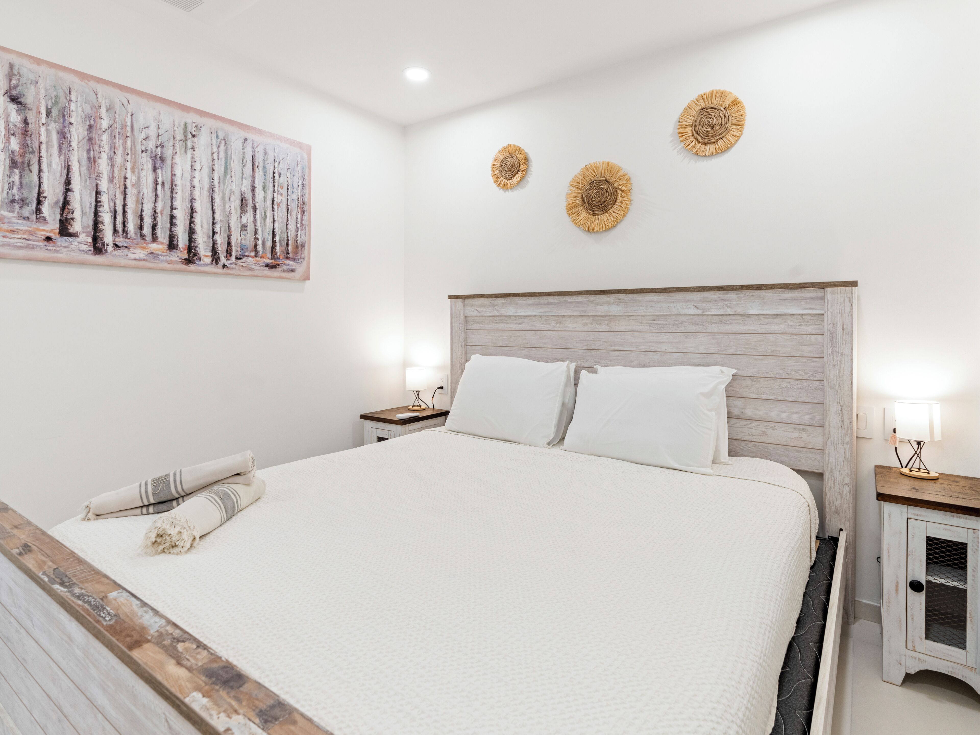A neatly arranged bedroom with a large bed, a wooden headboard, bedside tables with lamps, and a painting on the wall.