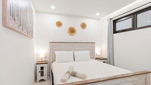 A modern bedroom with a wooden headboard, a large bed with white linens, two bedside tables with lamps, and decorative wall art. - A123 -  1 bedroom with paradise view (Sint Maarten)