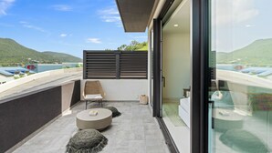 A modern balcony with a view of the sea and hills, featuring a wicker chair, round ottoman, and a glass door leading to a room. - B201 - Wonderfull Apartment with terrasse (Sint Maarten)