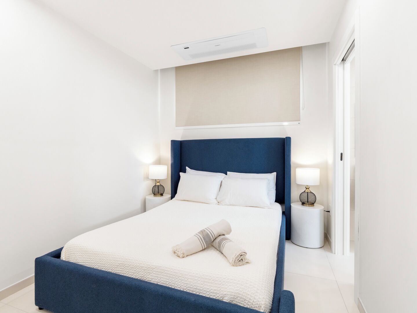 Une chambre d’hôtel moderne avec un grand lit, deux tables de chevet avec des lampes et un appareil de climatisation fixé au plafond.