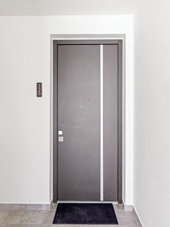 Una puerta moderna con una placa que indica la habitación 225, una cerradura electrónica y un felpudo en la entrada.