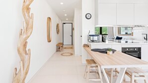 Una cocina moderna con armarios blancos, una mesa de comedor de madera y vistas al exterior con vegetación.