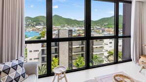 Habitación de hotel moderna con ventanas amplias que ofrecen vistas a un pueblo costero y montañas.