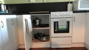 A compact kitchen with white cabinets, a built-in oven, and a microwave. - Beachend Bicheno (Bicheno)