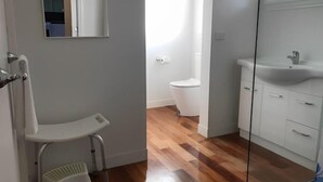 A bathroom with a white toilet, a sink, and a shower chair. - Beachend Bicheno (Bicheno)