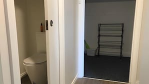 A narrow hallway with a white toilet and a black metal drying rack. - Beachend Bicheno (Bicheno)