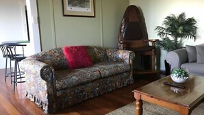 A living room with a floral sofa, a wooden coffee table, a red throw pillow, a framed picture on the wall, and a potted plant. - Beachend Bicheno (Bicheno)