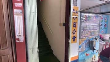 A staircase leading to an upper floor, a vending machine with beverages, and a door with a sign.
