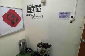 A door with a 'Welcome' sign, a red octagonal sign, and a metal shoe rack with shoes. - Pelangi Capsule Hostel (Johor Bahru)