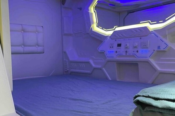 A futuristic room with a control panel, a padded headboard, and a blue floor.